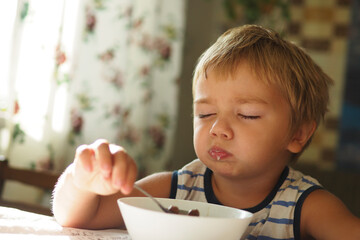 sleepy boy eating breakfast at the table with his eyes closed early in the morning..