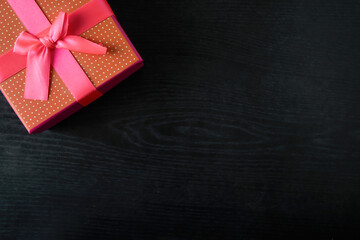 Red gift box with pink bow on the background of black wood. Place for text