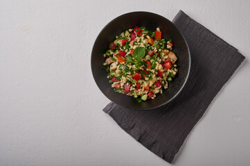 Middle Eastern traditional salad tabbouleh made of bulgur or couscous, poultry meat, parsley, mint in dark bowl with napkin on white background