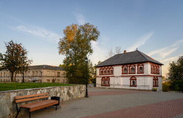 A public garden with an old red-and-white governor's house, a bench and a rowan tree in the...