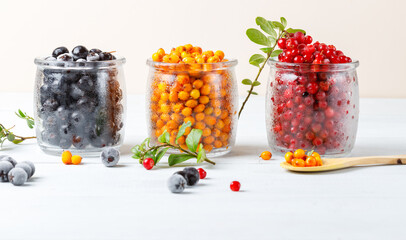 Three types of frozen bright wild berries in glass jars. Close-up, horizontal. Light background. © Mariia 
