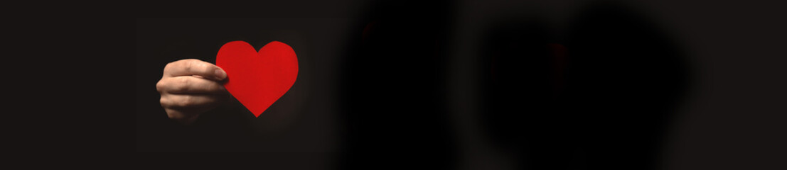 Wide web banner hand with red heart on black background. Concept of giving love, charity. Copy space photo