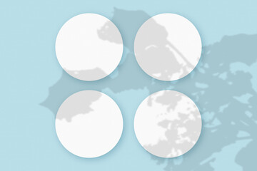 Mockup with vegetable shadows superimposed on 4 round sheets of textured white paper on a blue table background