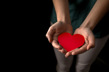 Young girl holding red heart on black background. Health insurance, organ donor day, charity concept. World health, mental and heart days concept. All lives matter photo