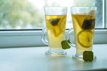 Close-up of couple of glasses on windowsill with vitamin green tea with lemon and orange. Tea bags.