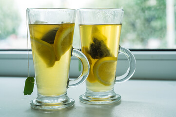 Close-up of couple of glasses on windowsill with vitamin green tea with lemon and orange. Tea bags.