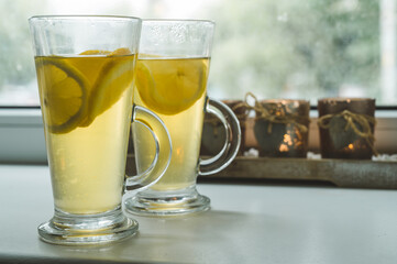 Close-up of couple of glasses on windowsill with vitamin green tea with lemon and orange. Candles on background.