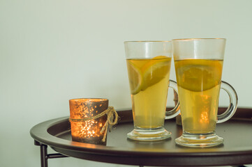 Couple of glasses with hot vitamine green tea with lemon and orange. Healthy drink against colds. Small candles.