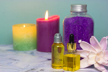 Obraz na płótnie Canvas Bottles with essential oil for hair, face and body care, violet lavender sea salt for bath in a bottle, burning candles in the background and pink lotus flower. Spa treatments. Cosmetic products.
