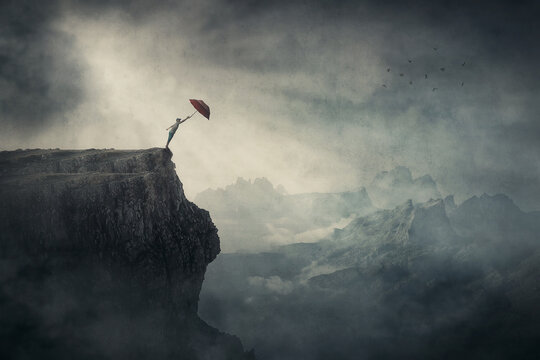 Fearless Person On The Edge Of A Cliff Determined To Catch His Umbrella And Fly Away Over Abyss. Surreal Adventure, Conceptual Scene For Achievement And Purposefulness