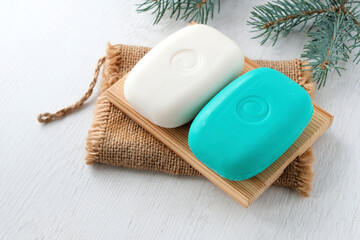 Obraz na płótnie Canvas White and green soap with pine needles extract on a wooden stand next to fir branches on a light background. Spa concept, beauty treatments