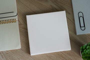 White empty square canvas for drawing lies on a wooden table next to a note. Mockup canvas (276)