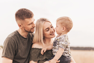 Beautiful family parents and a young son in a wheat field. Mom, Dad and Baby Together. Happy family, parents hugs their little son