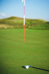 Obraz premium Golf ball and putter on the green grass next to the hole.