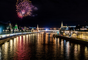 Fototapeta na wymiar fireworks over the night river with floating motor ships of the embankment and the old Kremlin 