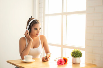 Asian woman wearing headphones using laptop sitting in her bedroom to communicate with friends during the epidemic of COVID-19