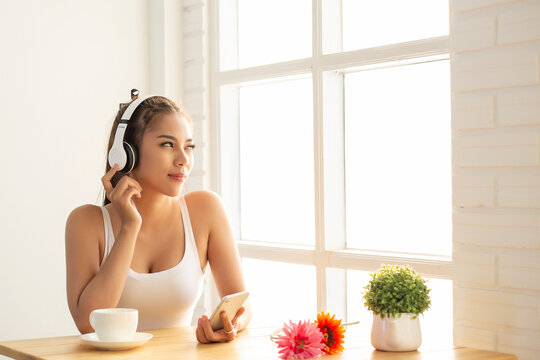 Asian woman wearing headphones using laptop sitting in her bedroom to communicate with friends during the epidemic of COVID-19
