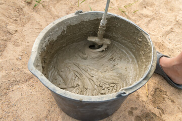 Fototapeta premium Mixing cement mortar in a bucket with an electric construction drill close-up