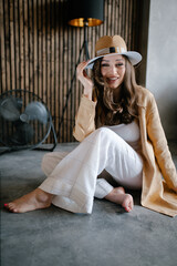 a beautiful girl with long hair in a jacket and a sand-colored hat and white trousers and a T-shirt...