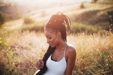 Beautiful black young woman in the park portrait long braids smiling flower
