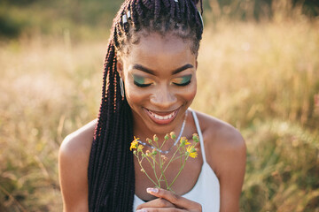 Beautiful black young woman in the park portrait long braids smiling flower bright makeup closeup