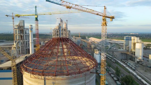 Aerial view of cement factory under construction with high concrete plant structure and tower cranes at industrial production area. Manufacture and global industry concept.