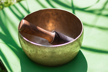 Antique bronze yoga bowl stands on green yoga mat in bright sun with hard shadows