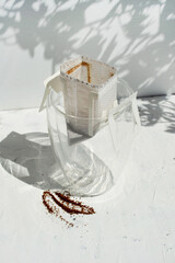 Glass cup with drip coffee bag on white background with shadow and copy space. Opened Instant paper sachet.