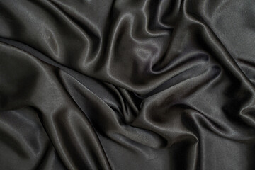 Black wavy silk background. Satin fabric texture. Dark elegant rich backdrop. Delicate design. Shine decoration christmas material. Tender art drape. Beautiful romantic textile