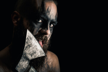 Viking warrior with black war paint, licking his axe. - obrazy, fototapety, plakaty