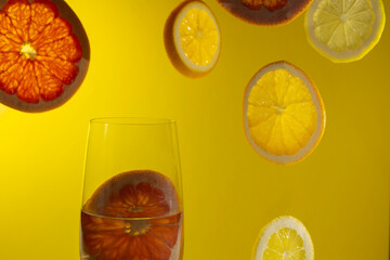 A closeup shot of a glass of water and orange and grapefruit slices against a yellow background
