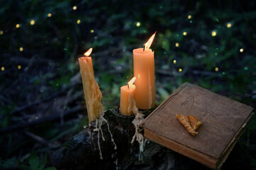 magic burning candles and old book in fabulous Night natural Background. mysterious fairy scene. witchcraft ritual. fall season. Samhain, Halloween holiday concept.