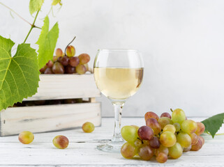 White wine in a transparent glass on the background of a wooden box with grapes