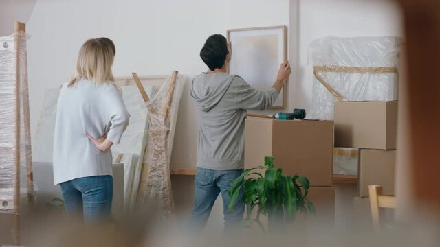 young couple moving into new house hanging picture on wall decorating home together enjoying teamwork in new apartment 4k footage