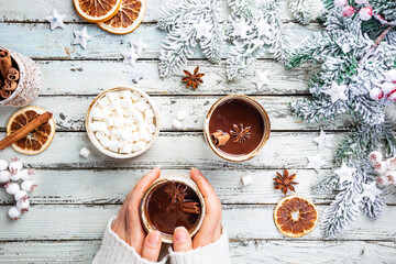 female hand holding cup of hot cocoa or chocolate on white wooden table, top view