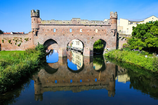 View over water canal on medieval watergate stone wall with 3 arches from 14th century with reflection against blue summer sky - Zutphen (Berkelpoort), Netherlands