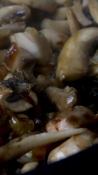 Finely chopped mushrooms are fried in pan in boiling vegetable or olive oil and mixed thoroughly with kitchen spatula. Domestic kitchen. Dolly shot. Vertical video. Close-up.