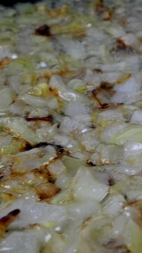 Finely chopped onions are fried in pan in boiling vegetable or olive oil. Domestic kitchen. Vertical video. Dolly shot. Close-up.