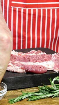Chef beats fresh raw slices pork meat with kitchen hammer before cooking on cutting board. Preparation smashing pork chops of steak. Sprinkle with spices. Vertical video. Dolly shot.