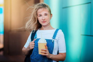 A beautiful young girl on the background of a turquoise wall holds a glass of coffee in the form of ice cream.