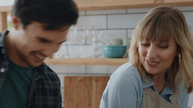 happy couple cooking in kitchen young man chopping vegetables with sneaky girlfriend stealing carrots smiling playfully enjoying fun preparing dinner together at home 4k footage