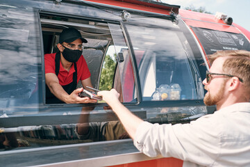 Young man holding smartphone over payment terminal while paying for fast food