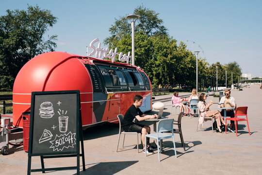 Several people spending time in outdoor cafe behind blackboard with announcement about discount