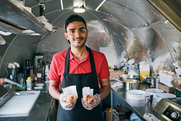 Gloved young man in uniform holding fast food while standing inside truck