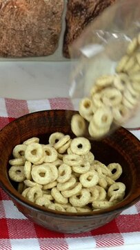 Fresh natural milk is poured in bowl with corn rings from pitcher, cage napkin. Nearby are jam, orange juice and cookie. Concept healthy cereal breakfast. Vertical video.