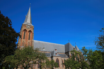 Fototapeta na wymiar View on dutch neo gothic church from 18th century with green trees against blue summer sky - Baak, Sint Martinuskerk, Netherlands