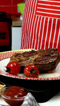 Chef decorates fried meat in plate with fried cherry tomatoes and rosemary. Vertical video. Close-up. Indoors.