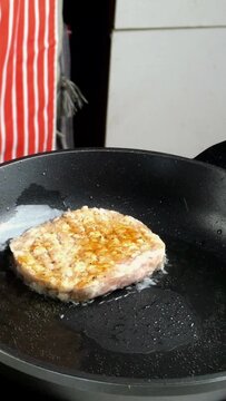 Chef prepares chicken cutlet for hamburger in domestic kitchen on kitchen table. Places minced meat in hot skillet with oil and garnish with rosemary sprigs. Vertical video.