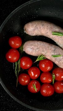 Fatty white bavarian sausages with tomato and sprig of rosemary fried in frying pan on electric stove. English or German, European or American breakfast. Top view. Vertical video.