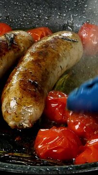 Fatty white bavarian sausages with tomato and sprig of rosemary are fried in frying pan on electric stove. English or German, European or American breakfast. Vertical video.